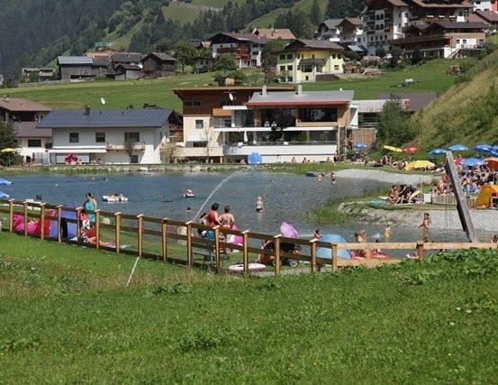 Eine malerische Ansicht eines Sees, umgeben von Häusern und Menschen, die an einem sonnigen Tag die Natur genießen.