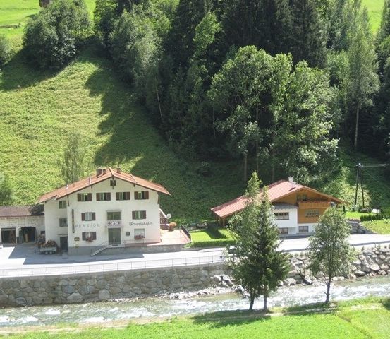 Eine Luftaufnahme eines Gästehauses mit rotem Dach, umgeben von üppigen grünen Hügeln und einem fließenden Fluss.