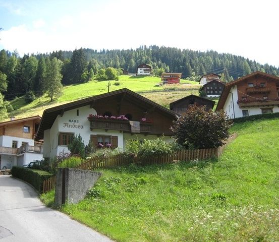 Ein Bergdorf mit mehreren Chalets, eines davon heißt Haus Andrea, umgeben von saftigem grünem Gras und Bäumen.