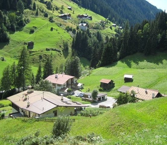 Luftaufnahme eines kleinen Dorfes in den Bergen mit mehreren Häusern und üppigen grünen Feldern.