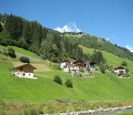Ein Hang mit mehreren Chalets, saftigem grünem Gras und einem Fluss im Vordergrund.