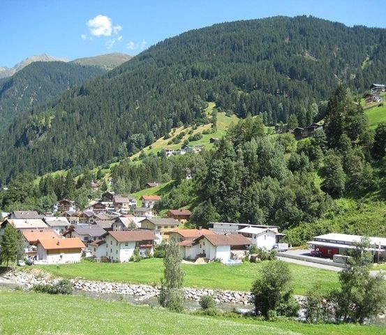 Ein malerisches Dorf in den Bergen mit üppigem Grün und klarem blauem Himmel.
