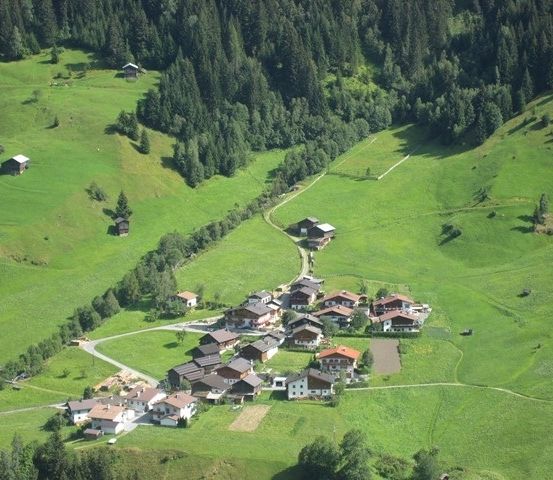 Eine Luftaufnahme eines kleinen Dorfes in einem üppig grünen Tal, umgeben von Kiefern und sanften Hügeln.