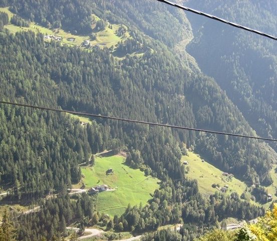 Eine szenische Luftaufnahme einer bergigen Region mit dichten grünen Wäldern, einer kurvenreichen Straße und einem kleinen Haus im Tal.
