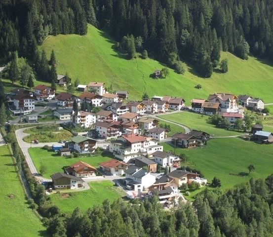 Luftaufnahme eines kleinen Dorfes in einem üppigen grünen Tal, umgeben von dichten Wäldern.