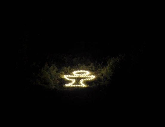 Ein leuchtendes Symbol, möglicherweise ein Kreuz, wird im Dunkeln mit einer Lichtquelle beleuchtet.