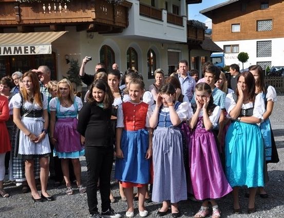 Eine Gruppe von Menschen, darunter junge Mädchen in traditioneller Kleidung, posiert für ein Foto vor einem Gebäude mit einem Schild, das Zimmer steht.