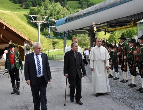 Eine Gruppe von Männern in traditionellen Uniformen steht in einer Reihe, während ein Mann in einem weißen Gewand und ein anderer Mann in einem Anzug an ihnen vorbeigeht.