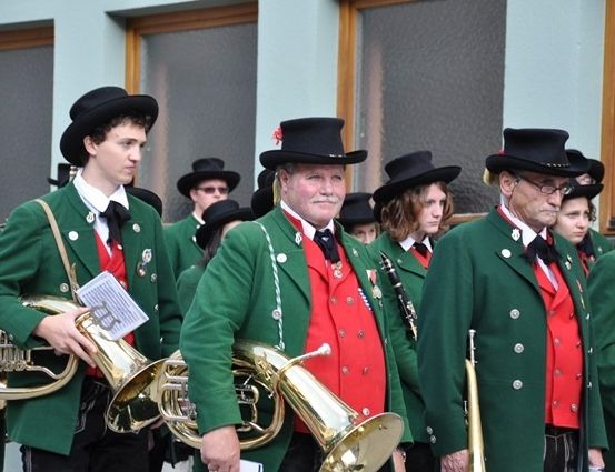 Eine Gruppe von Musikern in grünen und roten Uniformen, die Blechblasinstrumente halten, marschiert bei einer Parade.