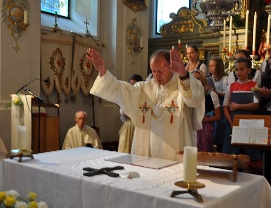 Ein Priester führt eine religiöse Zeremonie in einer Kirche mit Kerzen und Blumen auf dem Altar durch.