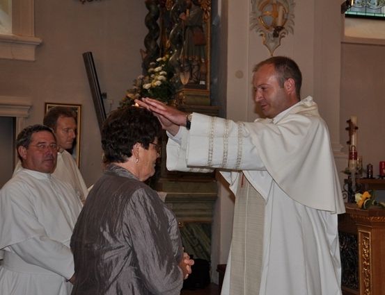 Ein Priester segnet eine Frau in einer Kirche, während andere Priester in der Nähe stehen.