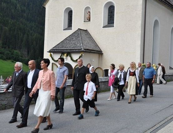 Eine Gruppe von Menschen, darunter Erwachsene und Kinder, geht auf einer Straße vor einer Kirche mit einer Statue an der Wand.