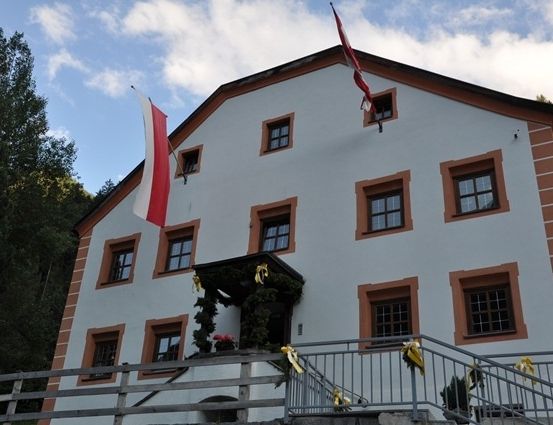 Ein weißes Gebäude mit braunen Verzierungen und mehreren Fenstern, geschmückt mit einer Flagge und Bändern, umgeben von Bäumen.