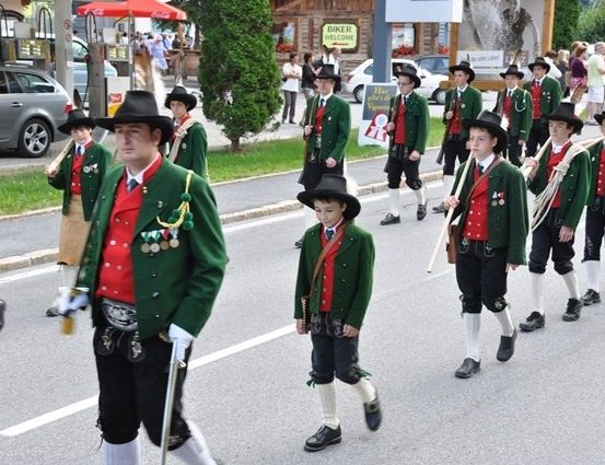 Eine Gruppe von Menschen in traditionellen grünen und roten Kostümen marschiert bei einer Parade auf einer Straße.
