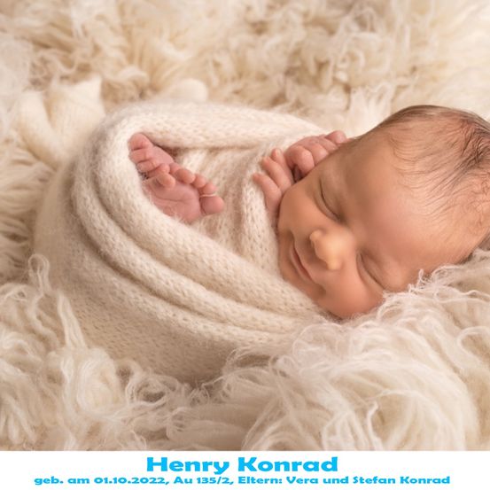 Ein Neugeborenes, Henry Konrad, geboren am 01.10.2022, schläft friedlich auf einer weißen Pelzdecke. Er ist in eine weiße Strickdecke gewickelt.