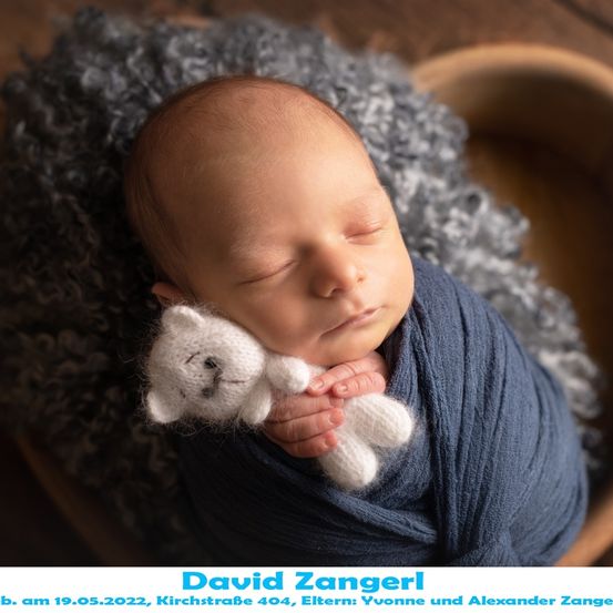 Ein Neugeborenes, David Zanger, geboren am 19. Mai 2022, schläft friedlich und hält einen weißen gestrickten Teddybären. Er ist in eine blaue Decke gewickelt.