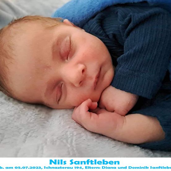 Ein neugeborener Junge, Nils Sanftleben, geboren am 5. Juli 2023, schläft friedlich auf einer weißen Decke. Er trägt ein blaues Langarmshirt und hat eine blaue Decke über sich.