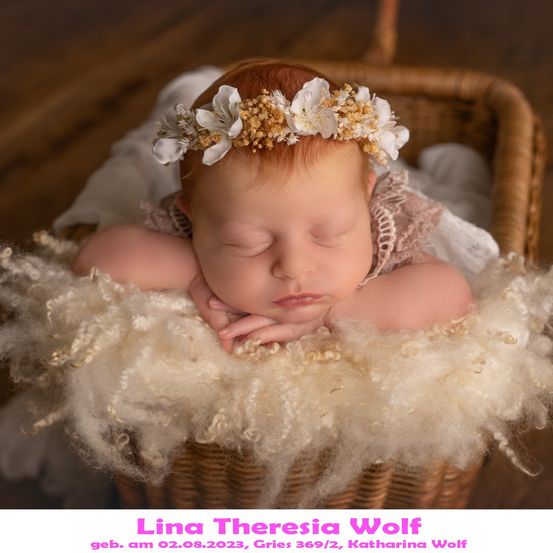 Ein schlafendes Babymädchen mit roten Haaren, das eine weiße Blumenkopfbinde trägt, liegt in einem mit weißer Wolle gefüllten Korb. Das Bild ist vom 2. August 2023.