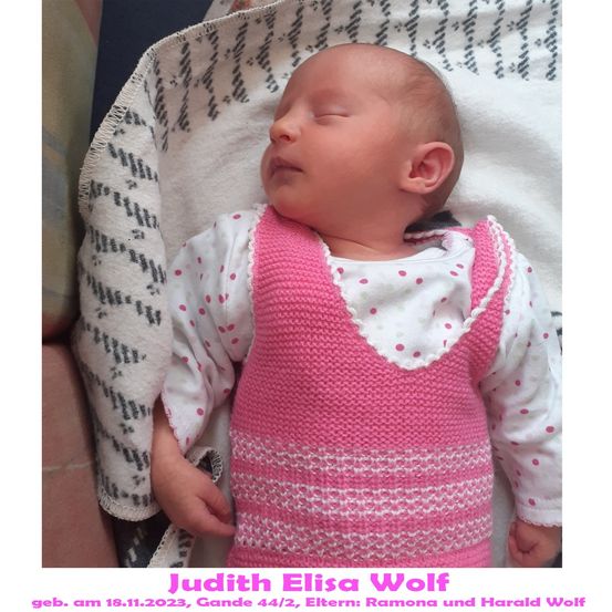 Ein Babymädchen schläft auf einer weißen Decke mit einem rosa gestrickten Westchen. Sie trägt ein weißes Langarmshirt mit rosa Punkten. Das Baby trägt ein rosa gestricktes Westchen mit weißen Punkten. Das Baby trägt ein weißes Langarmshirt mit rosa Punkten.