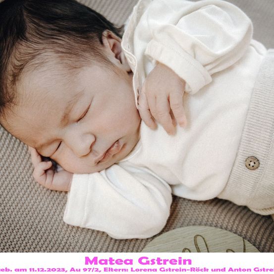 Ein Babymädchen namens Matea Gstrein, geboren am 11.12.2023, schläft friedlich auf einer weichen Oberfläche. Sie trägt ein weißes Outfit und hat ihre Hände sanft an ihr Gesicht gelegt.