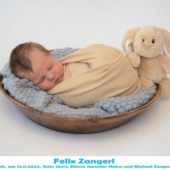 Ein Neugeborenes schläft in einer Holzschale, eingewickelt in eine beige Decke, mit einem Plüschhasen neben ihm. Das Bild ist vom 12. November 2024 und enthält den Namen des Babys, Felix Zangerl.