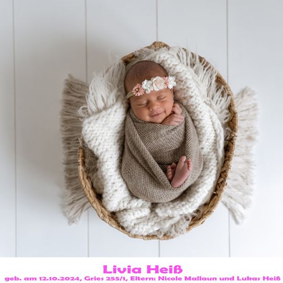 Ein neugeborenes Mädchen, Livia, in einer gewickelten Strickdecke schlafend in einem Korb mit einem rosa Blumenkopfband.