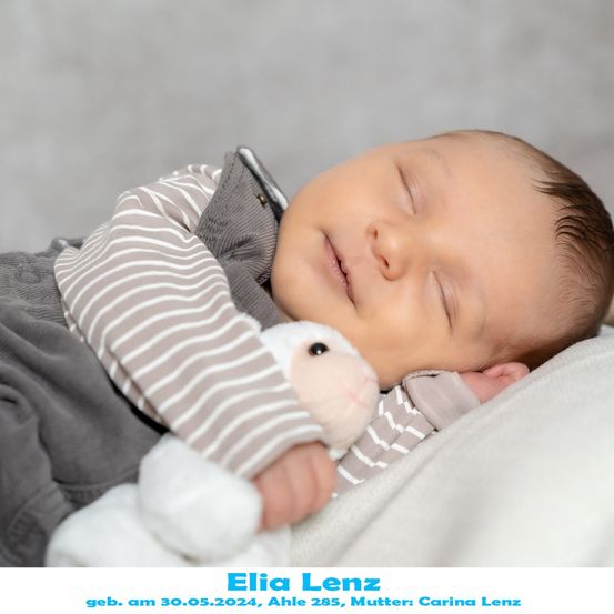 Ein schlafender Babyjunge, Elia Lenz, geboren am 30. Mai 2024, hält ein weißes Kuscheltier und liegt auf einer weißen Decke.