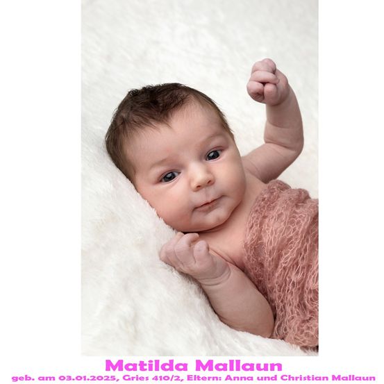 Ein neugeborenes Mädchen namens Matilda Mallaun, geboren am 3. Januar 2025, liegt auf einem weißen Pelzdecken und lächelt, während es mit der rechten Hand eine Faust macht.