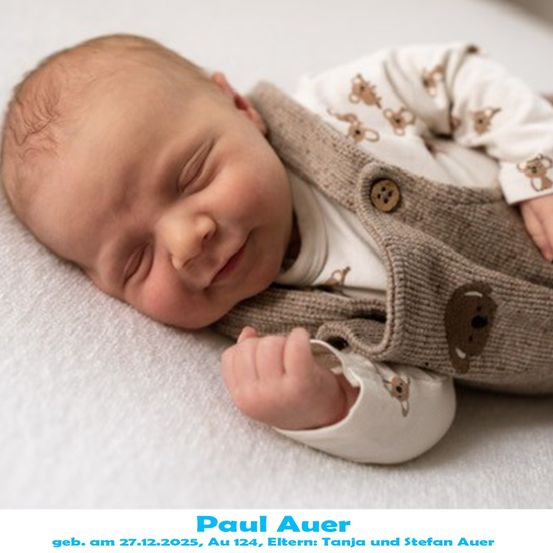 Ein Babyjunge namens Paul Auer, geboren am 27. Dezember 2025, liegt auf einer weißen Oberfläche, lächelt und trägt eine braune Weste mit Bärenmuster.