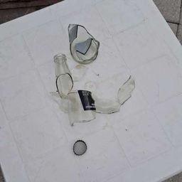 Ein weißer Plastiktisch mit zerbrochenen Glasflaschen und einem Verschluss auf dem Boden.
