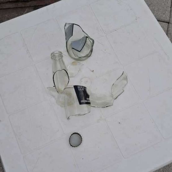 Ein weißer Plastiktisch mit zerbrochenen Glasflaschen und einem Verschluss auf dem Boden.