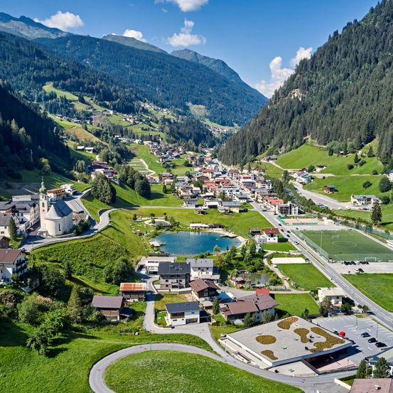 Luftaufnahme einer kleinen Stadt in den Bergen mit einem ruhigen See und einem Fußballplatz.