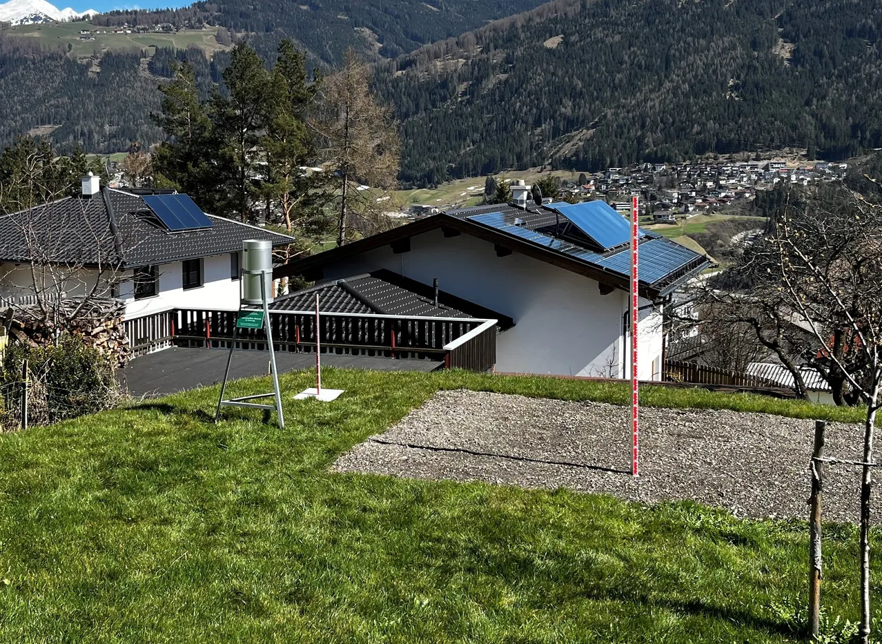 Zwei Häuser mit Solarpanelen auf ihren Dächern befinden sich auf einem Hügel mit Blick auf eine Stadt und Berge im Hintergrund.