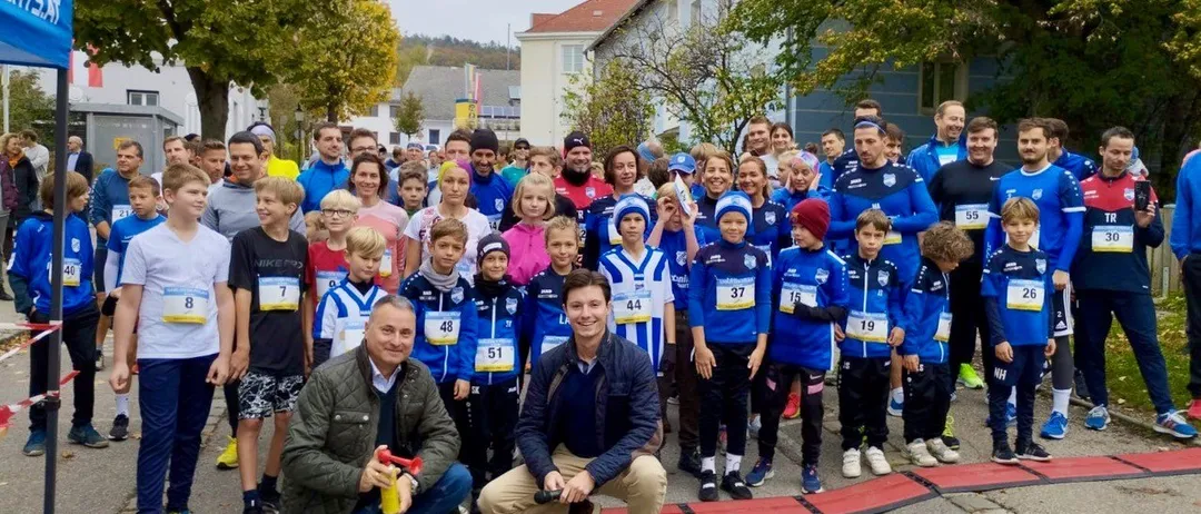 Eine Gruppe von Menschen, einschließlich Kinder, Erwachsene und zwei kniende Männer, posiert für ein Foto auf einer Straße vor Gebäuden.