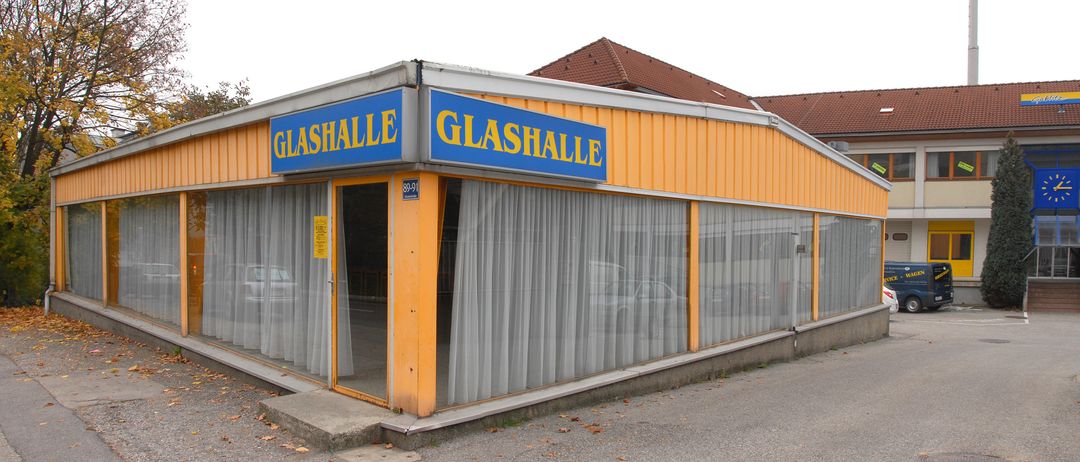 Ein gelbes Gebäude mit dem Wort Glashalle vorne und an der Seite. Das Gebäude hat große Fenster und ist mit Vorhängen verschlossen. Eine Nummer 89-91 befindet sich an der Tür.