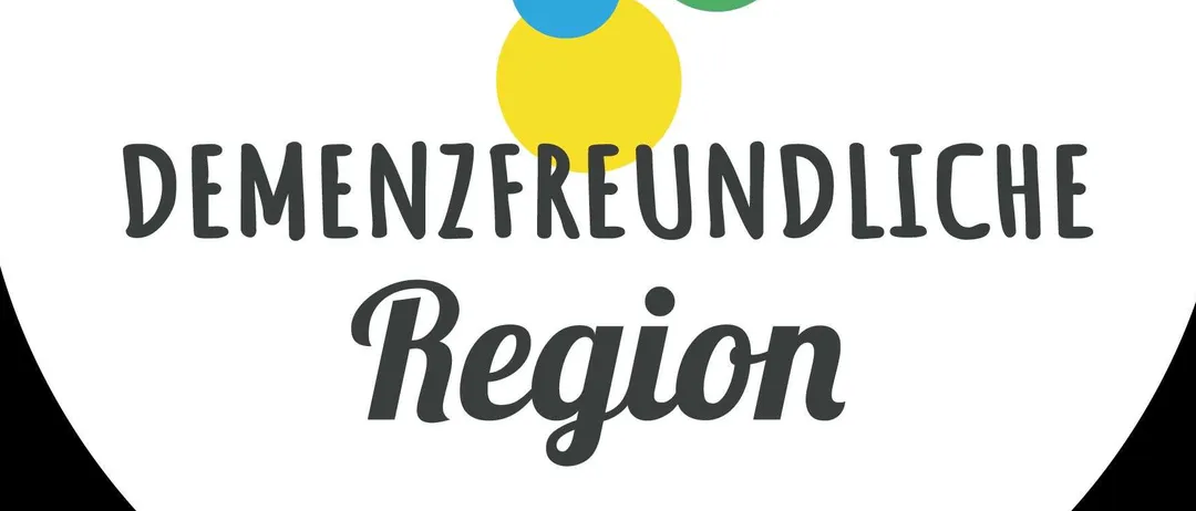 Ein weißes kreisförmiges Logo mit vier farbigen Kreisen und dem Text 'Demenzfreundliche Region'.