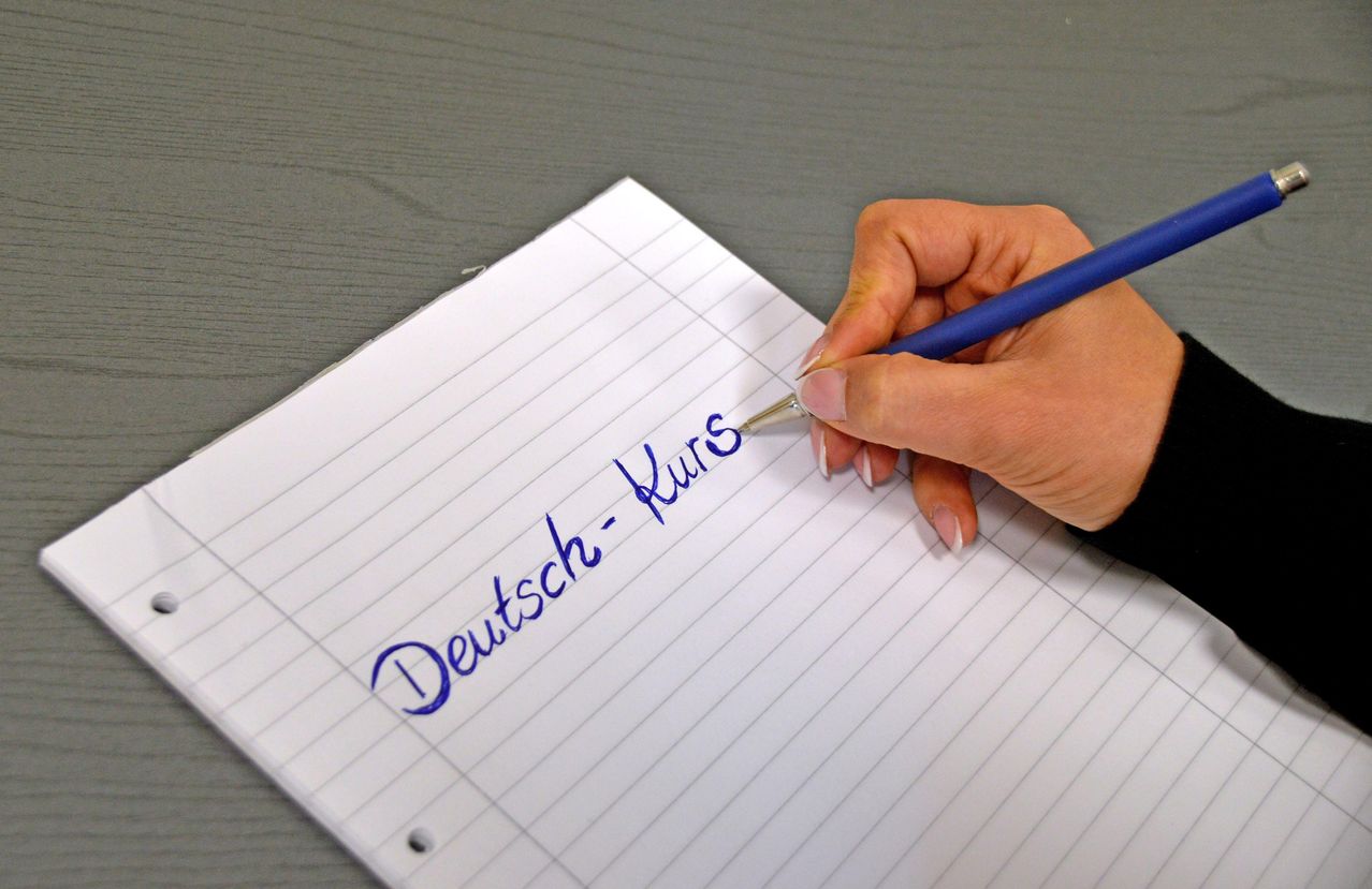 Eine Person schreibt auf einem Blatt Papier mit den Worten 'Deutsch Kurs' in blauer Tinte