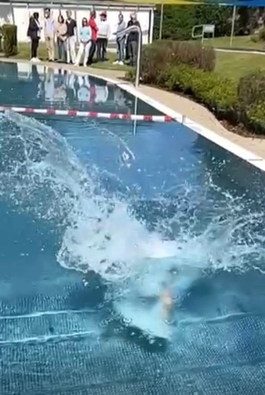 Ein Schwimmer taucht in einen Pool, wobei Wasser umherspritzt, beobachtet von einer Gruppe von Menschen am Poolrand.