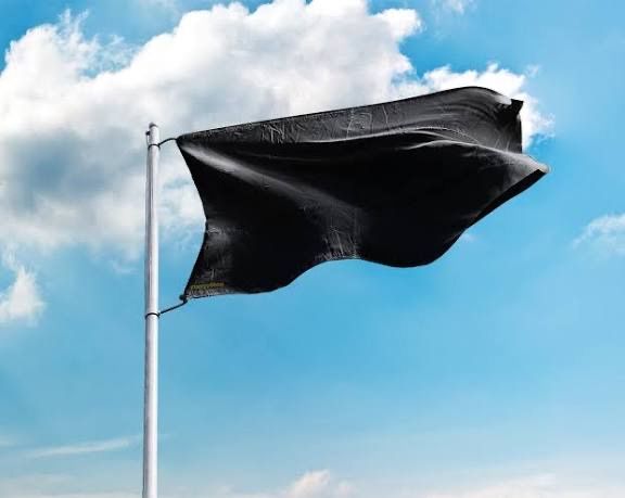 Eine schwarze Flagge weht auf einem Fahnenmast gegen einen klaren blauen Himmel mit verstreuten Wolken.