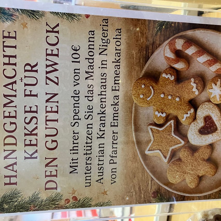 Das Poster zeigt einen Teller mit Weihnachtskeksen und Text darüber, der 'Handgemachte Kekse für den guten Zweck' lautet. Die Kekse sind mit Zuckerguss und Süßigkeiten verziert. Der Hintergrund ist hölzern.