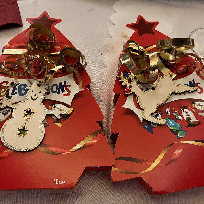 Zwei rote Geschenkboxen mit Weihnachtsdekorationen, eine mit einem Schneemann und die andere mit einem Rentier. Beide haben goldene Bänder und Süßigkeiten.