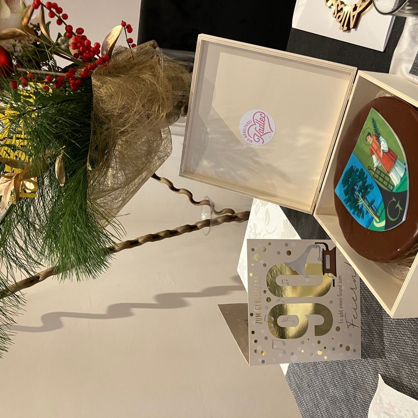 Ein Geburtstagskuchen mit einer religiösen Illustration in einer Schachtel, begleitet von einer dekorativen Pflanze und einer Geburtstagskarte.