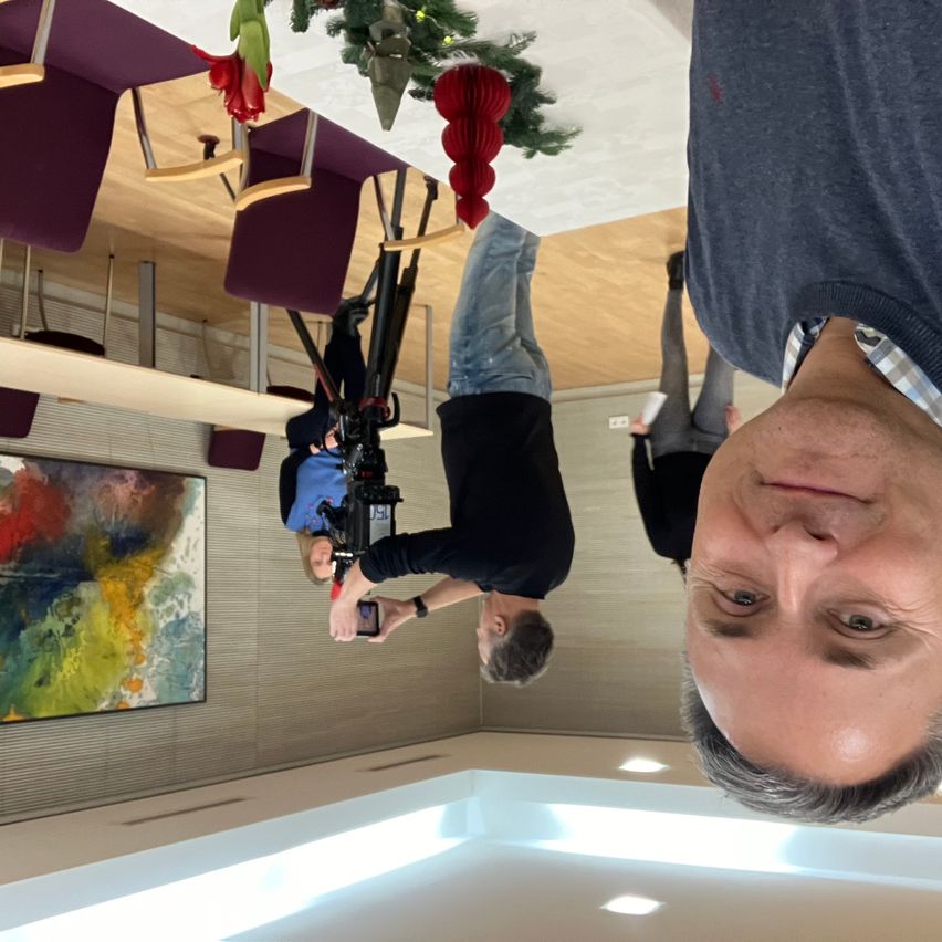 Ein Selfie mit einem Mann in einem blauen Hemd und einer Person, die eine Kamera hält, in einem Raum mit Weihnachtsdekorationen, die von der Decke hängen.