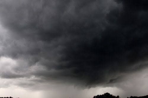 Ein dunkle, drohende Gewitterwolke kündigt Regen an, mit einem Hauch von Bäumen im Hintergrund.