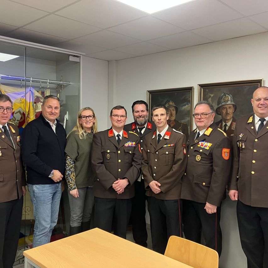 Eine Gruppe von Menschen in Uniform steht vor einer Wand mit zwei Gemälden. Eine Frau in der Mitte trägt eine Brille.