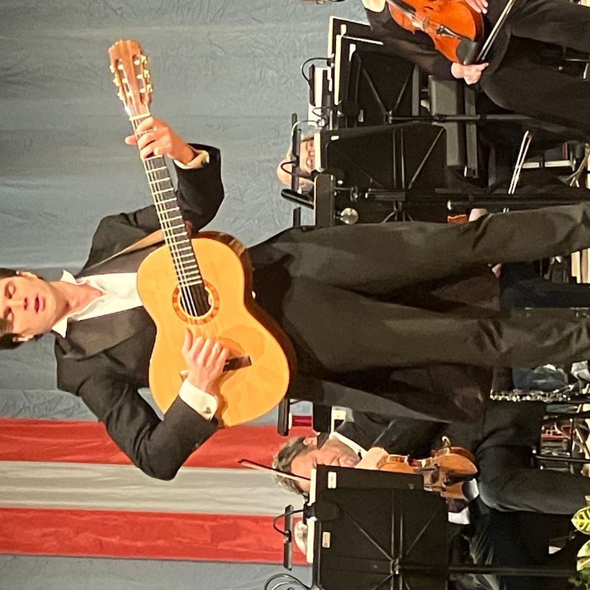 Ein Mann spielt Gitarre während einer Aufführung auf der Bühne, während ein anderer Musiker Geige spielt.