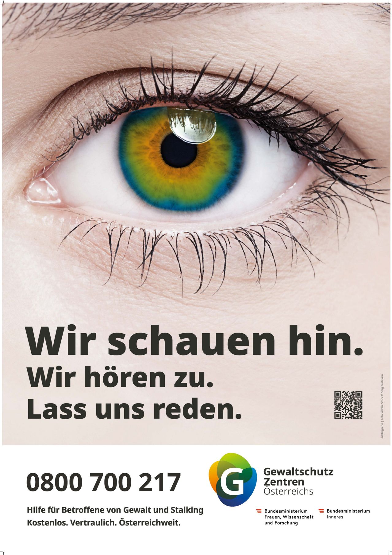 Nahaufnahme eines menschlichen Auges mit mehrfarbiger Iris. Der Text lautet: 'Wir schauen hin. Wir hören zu. Lass uns reden.' QR-Code unten rechts.