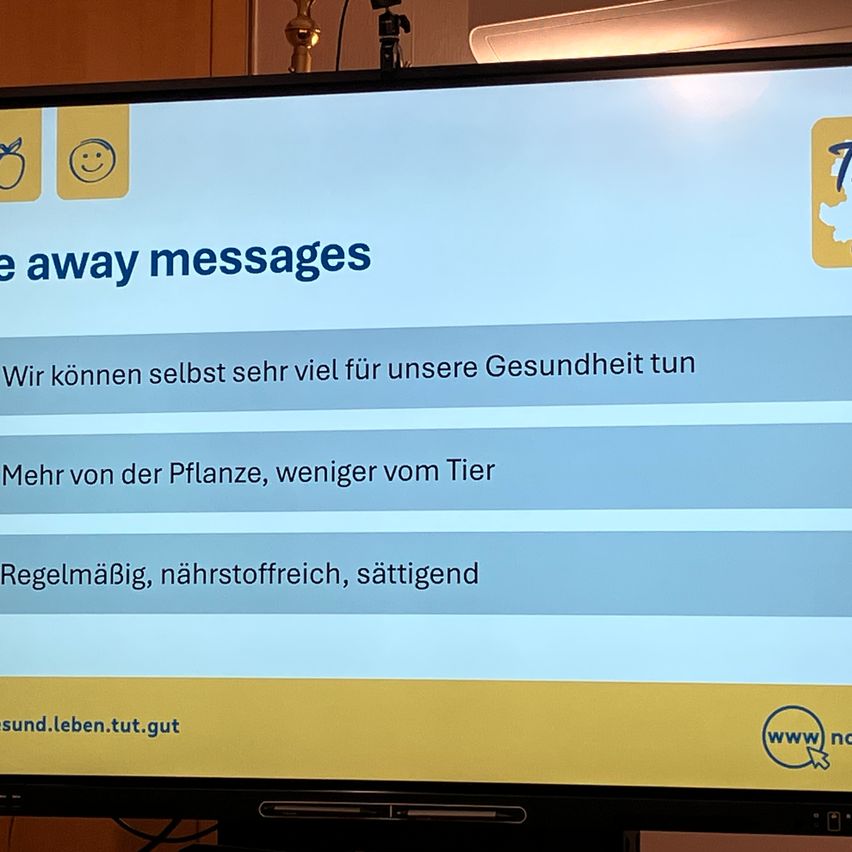 Ein Bildschirm zeigt '7 weg Nachrichten'. Darunter steht ein Text auf Deutsch: 'Wir können selbst sehr viel für unsere Gesundheit tun. Mehr von der Pflanze, weniger vom Tier. Regelmäßig, nährstoffreich, sättigend.' Eine Website-Adresse 'gesund.leben.tut.gut' ist angezeigt.