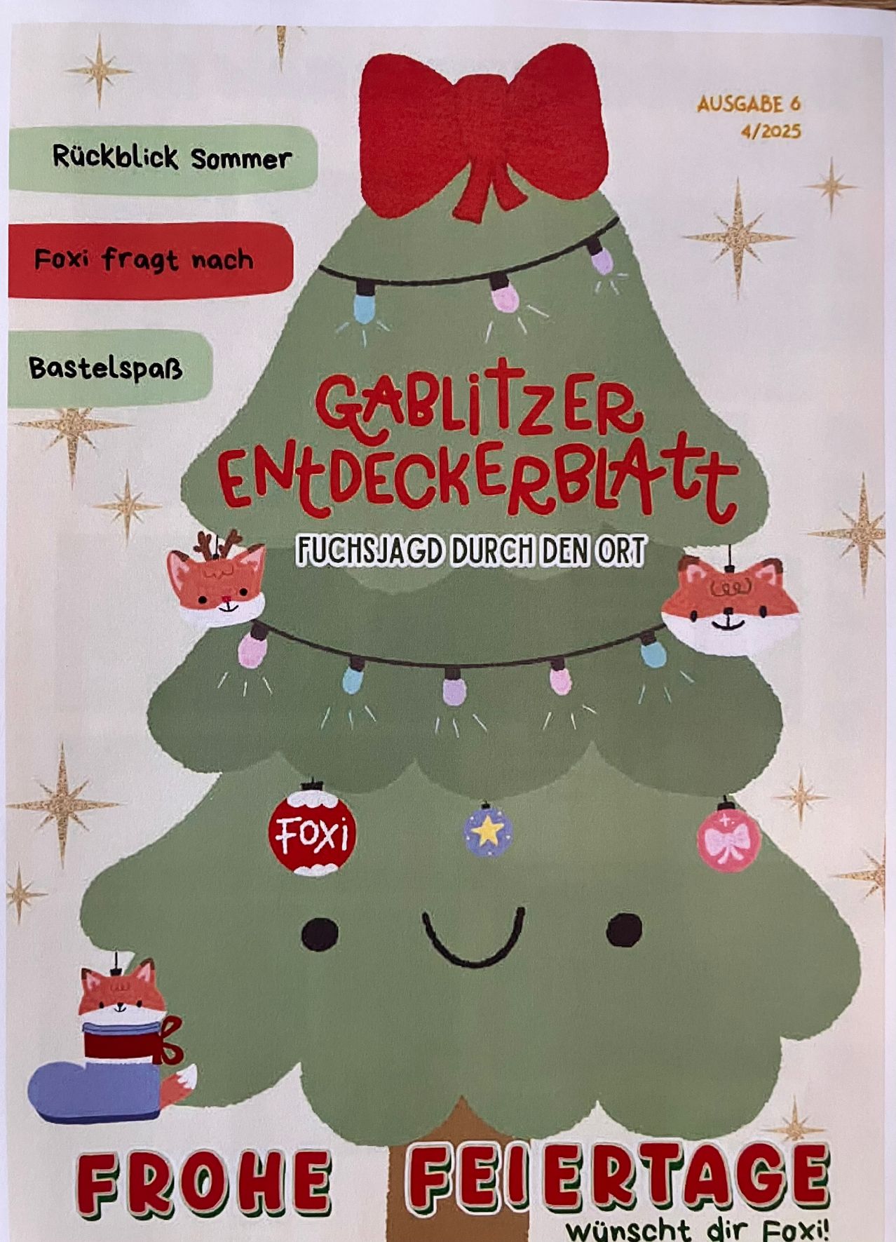 A cheerful Christmas tree with Foxi decorations, lights, and ornaments. The tree has a ribbon on top and a red banner that reads 'GABLITZER ENTDECKERBLATT'. Foxi is depicted with a cup of coffee.