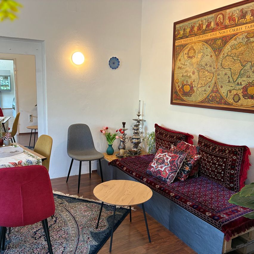 Ein Esszimmer mit einer Couch, einem Tisch und einer großen Karte an der Wand. Der Raum ist mit Stühlen und einem Tisch eingerichtet und die Couch ist mit farbenfrohen Kissen bedeckt.